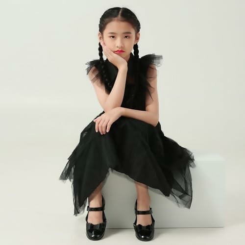 Young girl sitting in a black dress with braids.