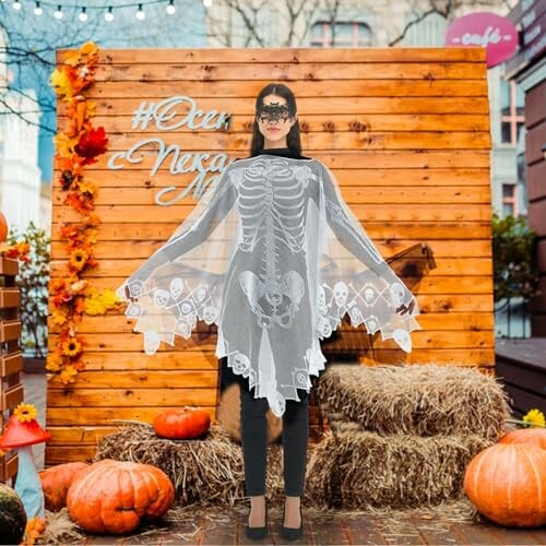 Person in skeleton costume standing in outdoor Halloween display with pumpkins and hay.